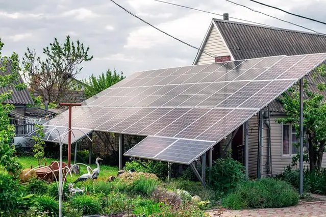 Panouri fotovoltaice pe o structură la sol, în grădina unei case de la țară